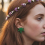 Close-up van een roodharige vrouw met een bloemenkrans die een felgroene oorsteker in de vorm van een cannabisblad (marihuanablad) draagt.