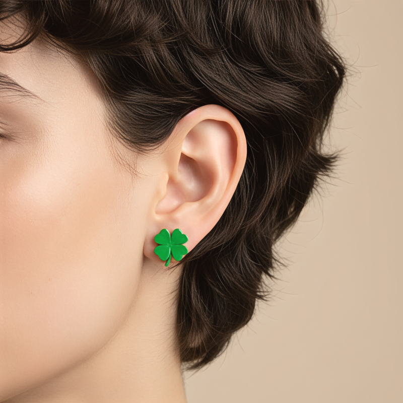 Close-up van een model met kort, donker haar dat een groene klavertje vier oorsteker draagt.