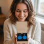 Vrouw Enthousiast over Gepersonaliseerde Oorbellen Cadeauset Lachende vrouw kijkt naar blauwe oorbellen met tekst in een houten cadeau doosje