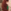 Close-up van het oor van een vrouw met golvend rood haar die een opvallende, felgroene oorbel in de vorm van een gekko draagt.