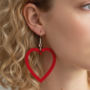 Close-up van het oor van een vrouw die een rode, uitgesneden hartvormige oorbel aan een zilveren haakje draagt.