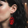 Rebellious Rode tongue Oorbel Close-up van een oor met meerdere piercings die een opvallende, rode loorbel in de vorm van het iconische 'Tong' logo draagt.