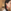 Close-up van het oor van een vrouw met een dikke, gevlochten staart die een rode oorbel in de vorm van een gedetailleerd anatomisch menselijk hart draagt.