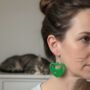 Groene Kattenhart Oorbellen TekstClose-up van een vrouw die een kleine, groene oorbellen draagt in de vorm van een kattenhoofd in een hartje