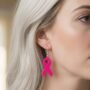 Pink Ribbon Oorbel Zilveren Haakje Blond Haar Fotorealistische close-up van een roze lint-oorbel aan een zilveren haakje, gedragen door een model met blond haar. Borstkanker bewustzijn juwelen.