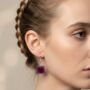 Lifestyle foto vierkante paarse oorbellen met bordeaux accent Close-up van een vrouw met gevlochten haar die een handgemaakte vierkante paarse oorbel draagt met een bruin rond kleuraccent in het midden