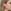 Close-up van een vrouw met blond haar in zijprofiel die een handgemaakte driehoekige oorbel draagt met een rood en transparant kleurverloop en een blauw accent.