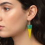 Close-up van een vrouw die een langwerpige driehoekige oorbel draagt met een kleurverloop van aqua groen naar felgeel