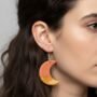 Productfoto van een Vrouw die Handgemaakte Oranje en Gele Maan Oorbellen Draagt Close-up van het zijprofiel van een vrouw met donker haar die een handgemaakte halve maan oorbel in terracotta en okergeel draagt.