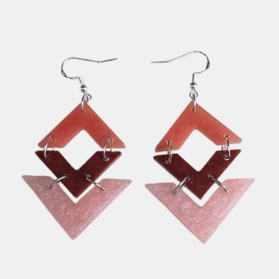 Handgemaakte geometrische oorbellen bestaande uit drie in elkaar grijpende ruitvormen in de kleuren terra, donkerbruin en lichtroze met een subtiele glitterafwerking aan zilverkleurige haakjes.