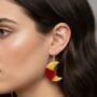 Model met Halve Maan Oorbellen Geel en Rood Marmer Close-up van een model met donker haar die handgemaakte halve maan oorbellen van geel en rood marmeren kunsthars draagt.