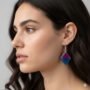 Handgemaakte ruitvormige epoxy oorbellen met paars-blauw kleurverloop gedragen door model Close-up van een vrouwelijk model met donker haar die een ruitvormige epoxy oorbel draagt met een tweekleurig verloop van paars naar blauw en glitters.