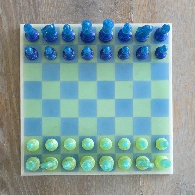 Handgemaakt-epoxy-schaakbord-blauw-groen. Modern handgemaakt schaakbord van hars in transparant blauw en limegroen op houten ondergrond bovenaanzicht.