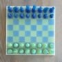 6.Modern-epoxy-schaakspel-perspectief-blauw-groen. Handgemaakt epoxy schaakbord met blauwe en limegroene transparante schaakstukken in schuin vooraanzicht op houten tafel.