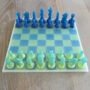 5.Modern-epoxy-schaakspel-perspectief-blauw-groen. Handgemaakt epoxy schaakbord met blauwe en limegroene transparante schaakstukken in schuin vooraanzicht op houten tafel.