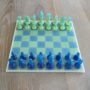 4.Modern-epoxy-schaakspel-perspectief-blauw-groen. Handgemaakt epoxy schaakbord met blauwe en limegroene transparante schaakstukken in schuin vooraanzicht op houten tafel.