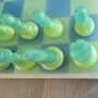 1.Modern-epoxy-schaakspel-perspectief-blauw-groen. Handgemaakt epoxy schaakbord met blauwe en limegroene transparante schaakstukken in schuin vooraanzicht op houten tafel.