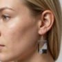 Close-up van een model met blond haar dat een handgemaakte rechthoekige epoxy oorbel draagt met zwart en witglitter effect