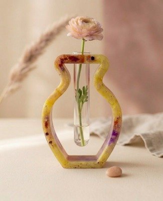 Handgemaakt-geel-epoxy-vaasje-enjoykado Handgemaakt geel epoxy vaasje met glazen reageerbuis en een roze bloem op een beige ondergrond.