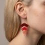 Geometrische Chevron Glitter Oorbellen - Kleurverloop Rood-Roze Een close-up van een vrouwelijke model met blond haar dat achter haar oor is gestoken, waardoor de handgemaakte chevron glitter oorbellen in een rood-tot-roze kleurverloop goed zichtbaar zijn.