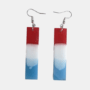 Handgemaakte rechthoekige hars oorbellen met een verticaal kleurverloop in rood, wit en blauw aan zilverkleurige oorhaakjes.