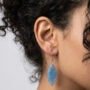 Close-up van een model dat een handgemaakte lichtblauwe bladvormige oorbel van hars draagt met zilverkleurige details