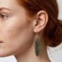 Close-up van een vrouw met opgestoken haar die een handgemaakte ovale olijfgroene oorbel van hars draagt