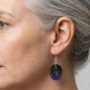 model-draagt-epoxy-oorbellen-groen-paars Zijaanzicht van een vrouw die een handgemaakte ovale epoxy oorbel draagt met een glinsterend groen en paars kleurverloop aan een zilveren haakje.