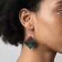 Close-up zijaanzicht van een model met donker kroeshaar die een handgemaakte ruitvormige epoxy oorbel draagt in bruin en groen met glitters