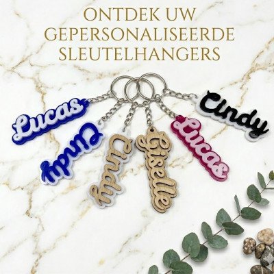Zes verschillende gepersonaliseerde sleutelhangers met namen zoals Lucas, Cindy en Giselle in diverse kleuren en materialen zoals hout, blauw, roze en zwart op een marmeren achtergrond.