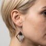 Close-up van een model met kort blond haar die handgemaakte geometrische epoxy oorbellen draagt met zwart en wit glitter verloop