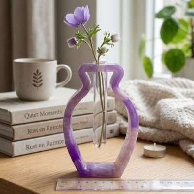 epoxy-vaas-paars-marmer-look-enjoykado Handgemaakte paarse epoxy vaas met glazen reageerbuis op een houten tafel naast boeken en een kopje thee