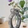 Handgemaakte grijze epoxy vaas met een gemarmerde beton-look en een kunststof reageerbuis met paarse bloemen op een houten tafel