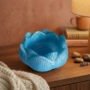 Blauwe epoxy lotusbloem waxinelichthouder Handgemaakte lichtblauwe epoxy waxinelichthouder in de vorm van een lotusbloem op een houten dressoir