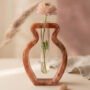 Een organisch gevormde koperkleurige epoxy propagation vaas met een glazen reageerbuis waarin een roze ranunculus bloem staat op een lichte ondergrond.